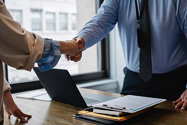 two people shaking hands over a laptop